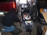 Mary in her Jeep stroller leaning over the side to watch daddy pumping up the tires.