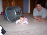 Mary on the floor with the empty laundry basket tipped on it's side next to her. Daddy is behind her smiling at the camera.