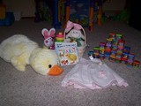 Mary's easter gifts, A big plush chickie, some stackable rings, an easter basket, some books, a dress, and some blocks.