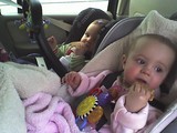 Kate and Mary sitting in their car seats each eating a graham cracker.