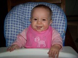 Mary sitting in her highchair with a smile and baby cereal all around her mouth.