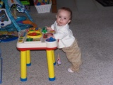 Mary standing at her play table looking sideways towards the camers.