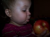 Mary with a bite of apple in her mouth staring intently at the apple.