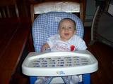 Mary sitting in her highchair smiling, maouth open, up at the camera.  She is wearing her 'I Love My Daddy' shirt.