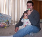 Daddy sitting on the floor with Mary in his lap.  Both are eating marshmallow Peeps.