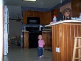 Mary standing in the middle of the kitchen crying while mommy is bent over the counter filling something out.