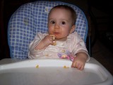 Mary siting in her high chair eating a graduate finger food.