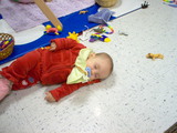 Mary laying in the middle of the floor in daycare asleep on her side surrounded by toys.