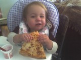 Mary in her highchair eating pizza.