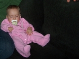 Mary, asleep, propped up next to daddy with her right arm on his left leg slumped forward on the couch with her binkie in her mouth.
