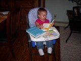 Mary sitting in her highchair reading a book.