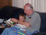 Mary and Papa sitting on the couch reading books.  Papa has 10 books stacked on his lap.