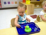 Mary sitting at her table playing with a rubber ducky in a bath of water.