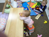 Mary standing at the bench in daycare with her feet inside a cloth box.