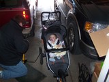 Mary sitting in her Jeep stroller while daddy pumps up the tires.