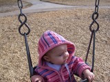 Mary in her pink jacket with her hood up in a little kid's swing.
